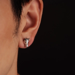 Detailed close-up of a vintage horse head stud earring on ear with intricate textures