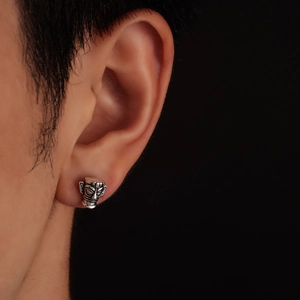 Close-up of retro Sanxingdui face mask stud earring worn on ear with silver finish