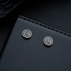 Macro detail of vintage silver lion head embossed stud earrings on black leather texture