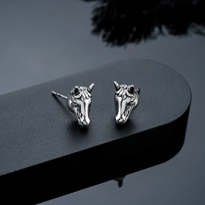 Macro shot of vintage silver horse head earrings with detailed relief on a dark pedestal