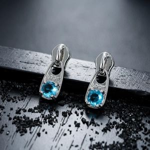 Boucles d'oreilles zip uniques avec zircon bleu sur un fond noir texturé