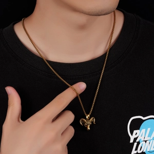 Detailed view of a gold ram head pendant on a round box chain worn by a model