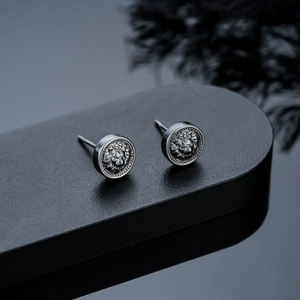 Detailed macro view of vintage lion head embossed silver stud earrings on a dark display