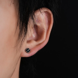 Close-up of a silver four-leaf clover stud earring with black enamel on a human ear