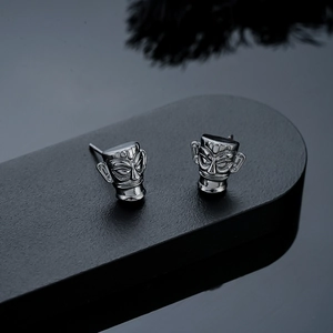 Close-up of vintage bronze mask stud earrings with antique black plating and sharp metallic texture