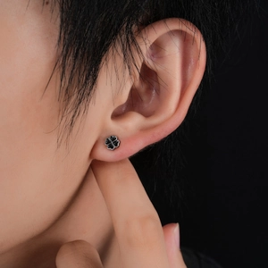 Close-up of a four-leaf clover stud earring in silver and black enamel worn on the ear
