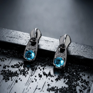 Détail macro de boucles d'oreilles zip en métal noir avec zircons bleus et gravure