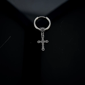 Macro detail of a vintage silver cross pendant earring with ornate engraved patterns