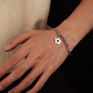 Close-up of asymmetric stainless steel chain bracelet with minimalist floral charm