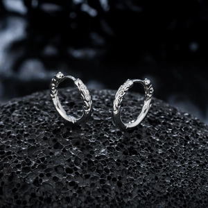 Silver hoop earrings with vintage embossed patterns on black volcanic rock background