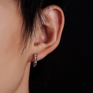 Close-up of silver twist hoop earring worn on ear with minimalist braided metal texture