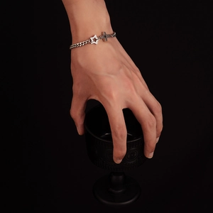 Detail of punk silver Cuban chain bracelet with star and cross charms on a male wrist