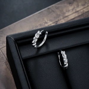 Macro detail of silver rope twist hoop earrings on black leather texture jewelry display