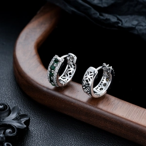 Détail macro de créoles en argent avec zircons verts et motifs étoilés ajourés sur le côté