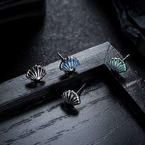 Minimalist shell-shaped metal stud earrings in four colors on a black frame background