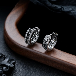 Vue macro de boucles d'oreilles huggie argentées avec pierres noires et fleurs