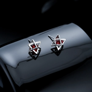 Close-up of silver hexagram stud earrings with red zircon stones on reflective surface