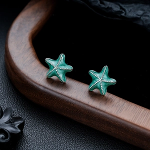 Detailed shot of mint green starfish stud earrings on a curved wooden stand