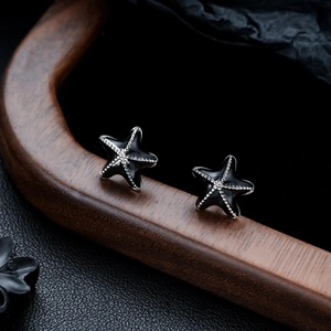 Macro shot of stylish black enamel starfish stud earrings with silver beaded texture
