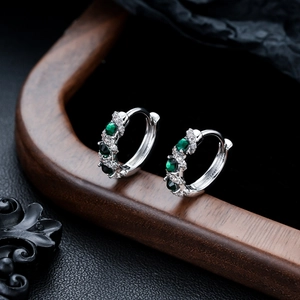 Macro shot of silver hoop earrings with emerald green gemstones and cubic zirconia accents