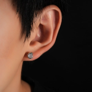 Macro shot of silver snake-shaped stud earring with clear crystal and green accents