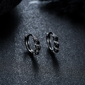 Macro detail of dark metal hoop earrings set with black and white pavé zircon stones