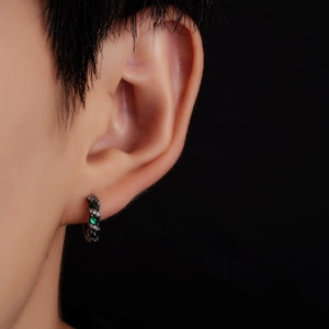 Macro side view of a braided hoop earring with emerald and clear zircon stones on ear