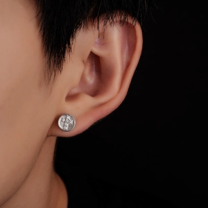 Gros plan d'une boucle d'oreille croix en argent avec zircons sur un disque en métal