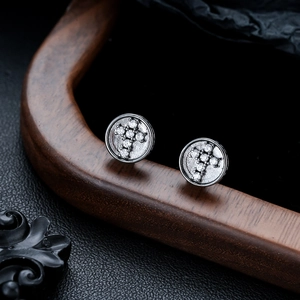 Détail macro de boucles d'oreilles croix en métal gris avec zirconiums sur bois et cuir