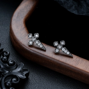 Macro shot of punk cross earrings with white zircon stones on dark silver metal