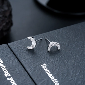Macro shot of silver crescent moon stud earrings with white zircon on black gift box
