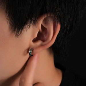 Close-up of silver huggie hoop earrings with vintage green enamel leaf pattern on model