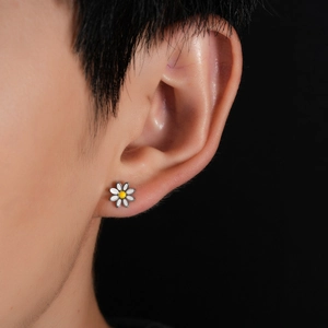 Close-up of small daisy stud earring with white petals on ear shown against dark background