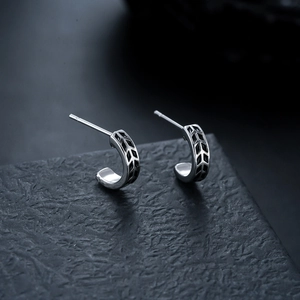 Macro view of C-shaped silver earrings with black geometric arrow textures on dark stand