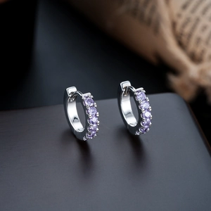 Macro shot of silver huggie earrings with round purple zircon stones on a wooden surface