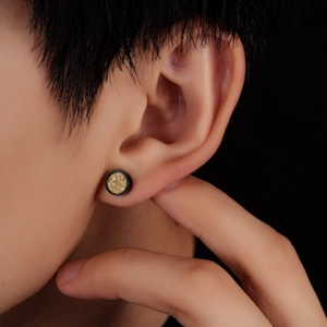 Macro view of black round titanium stud earring with golden textured center on ear