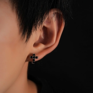 Close-up of a silver cross earring set with black round zircon stones on a female ear