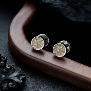 Detailed close-up of round titanium steel studs with gold textured inlay on a wood stand