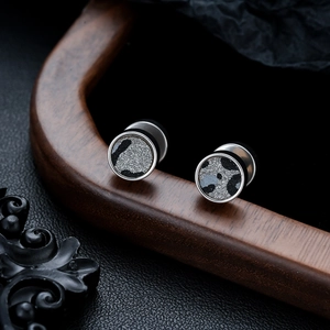Macro detail of silver titanium earrings with dark camouflage patterns on wood stand