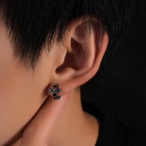 Macro shot of cross earring with black zircon stones and dark metallic finish on ear