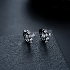 Macro shot of black plated cross huggie earrings with cubic zirconia stones on stone surface