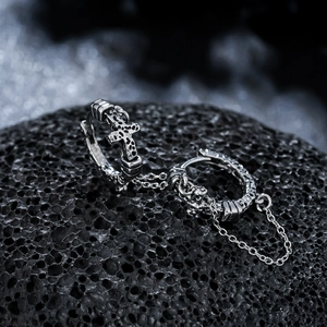 Détail de boucles d'oreilles croix et crâne gothiques avec chaîne sur pierre noire