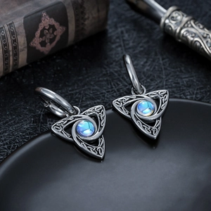 Détail de boucles d'oreilles triangulaires en acier titane avec nœud celtique et gemme
