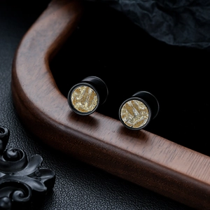 Macro detail of matte black titanium steel ear plugs with intricate golden woven texture