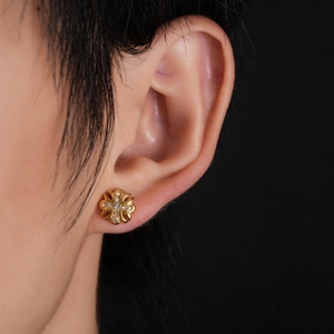 Close-up of golden fleur-de-lis cross stud earrings with zircon stones on model ear