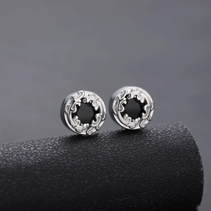 Close-up of vintage round stud earrings with silver engraved patterns and black center stone