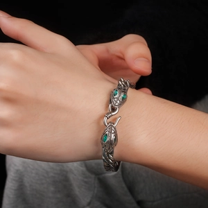 Macro detail of silver stainless steel snake head bracelet with green gemstone eyes