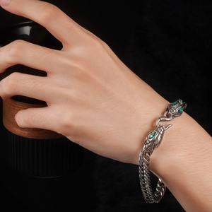 Detailed view of silver snake head clasp with green gemstone eyes on men's chain bracelet
