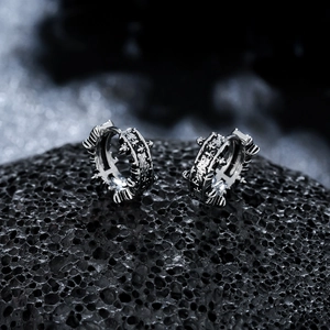 Macro shot of retro titanium steel earrings with irregular rock texture on dark volcanic rock