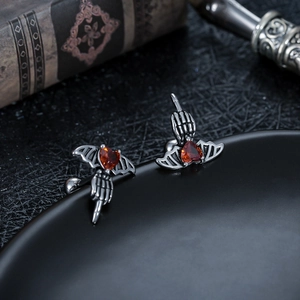 Macro shot of gothic wing stud earrings with a red heart gem and skeleton hand detail